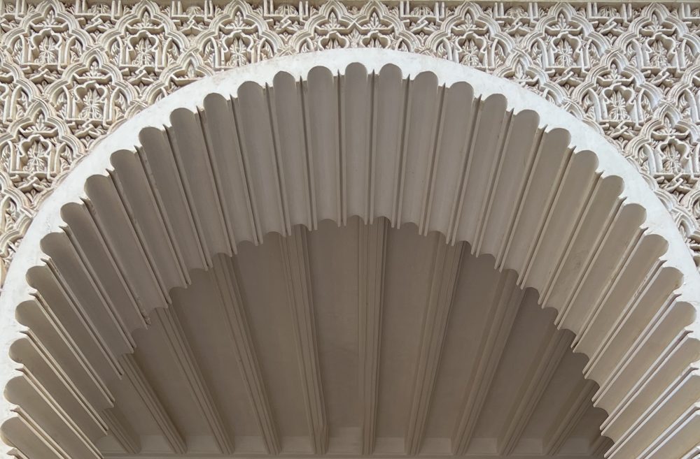 A close-up of a scalloped archway carved with intricate geometric plasterwork.