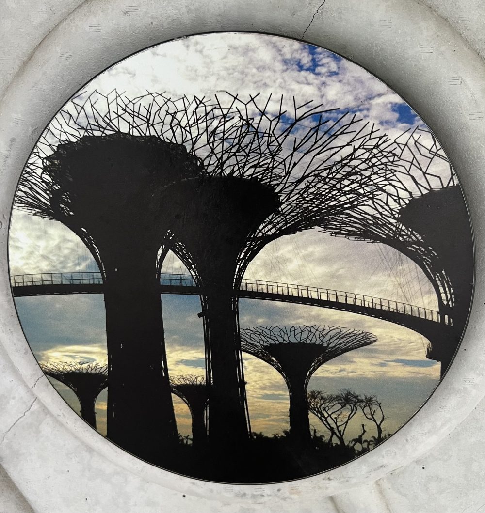 A circular stone porthole framing a silhouette of Supertree Grove's towering structures at dusk, Gardens by the Bay.