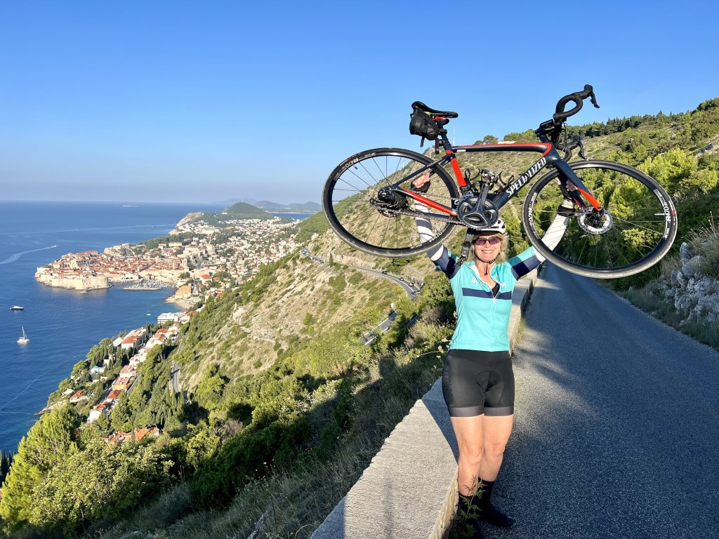 cyclist holding up road bike on side of the road overlooking the city of Dubrovnik in celebration of her 16 day Venetians cycling tour from Venice to dubrovnik