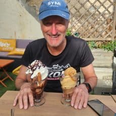 Bike Odyssey guest Glen Greedy in a blue cap, smiling over two ice cream sundaes at a café table after a ride.
