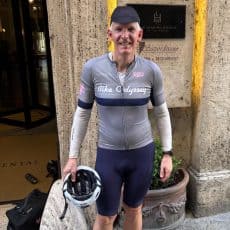 Bike Odyssey guest Scott Henderson in a Bike Odyssey cycling jersey, holding his helmet outside a hotel on tour.